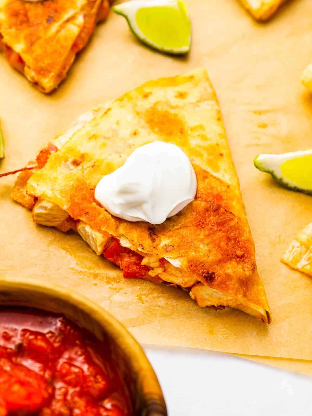 a chicken quesadilla topped with sour cream on parchment paper.