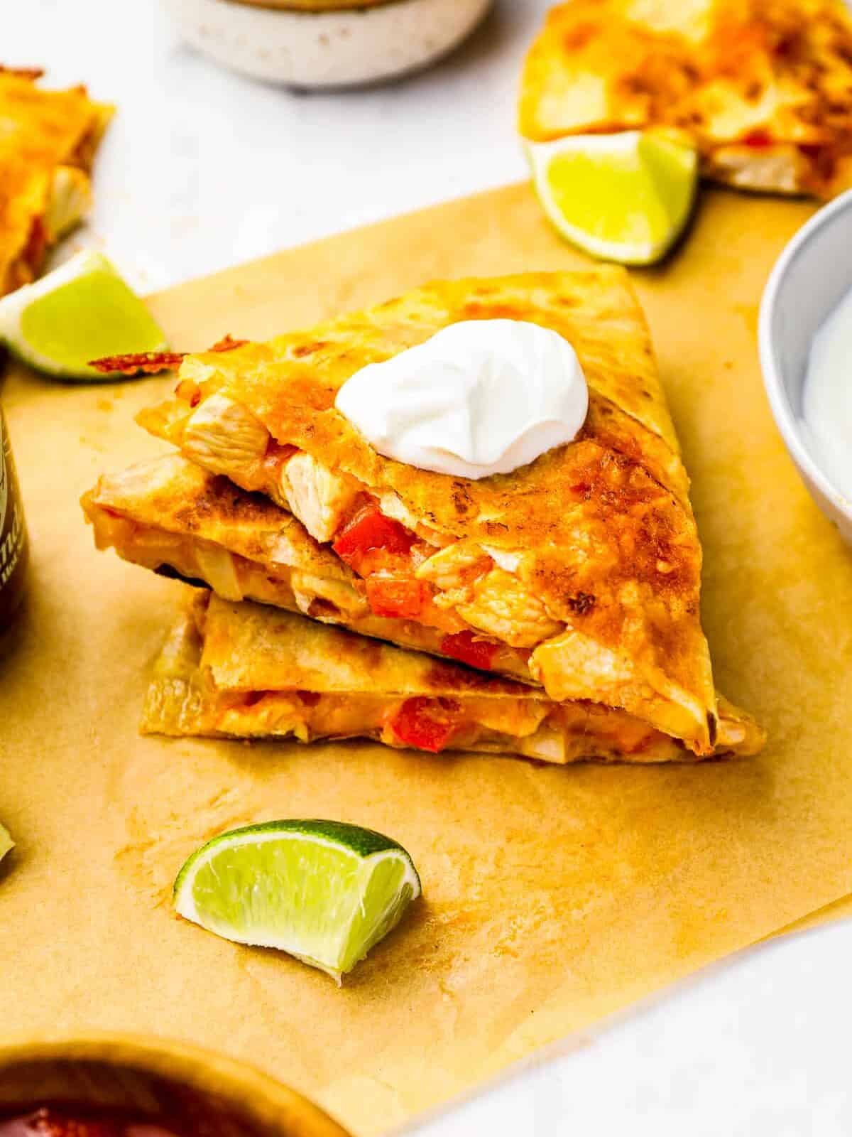 chicken quesadillas stacked on parchment paper with limes.
