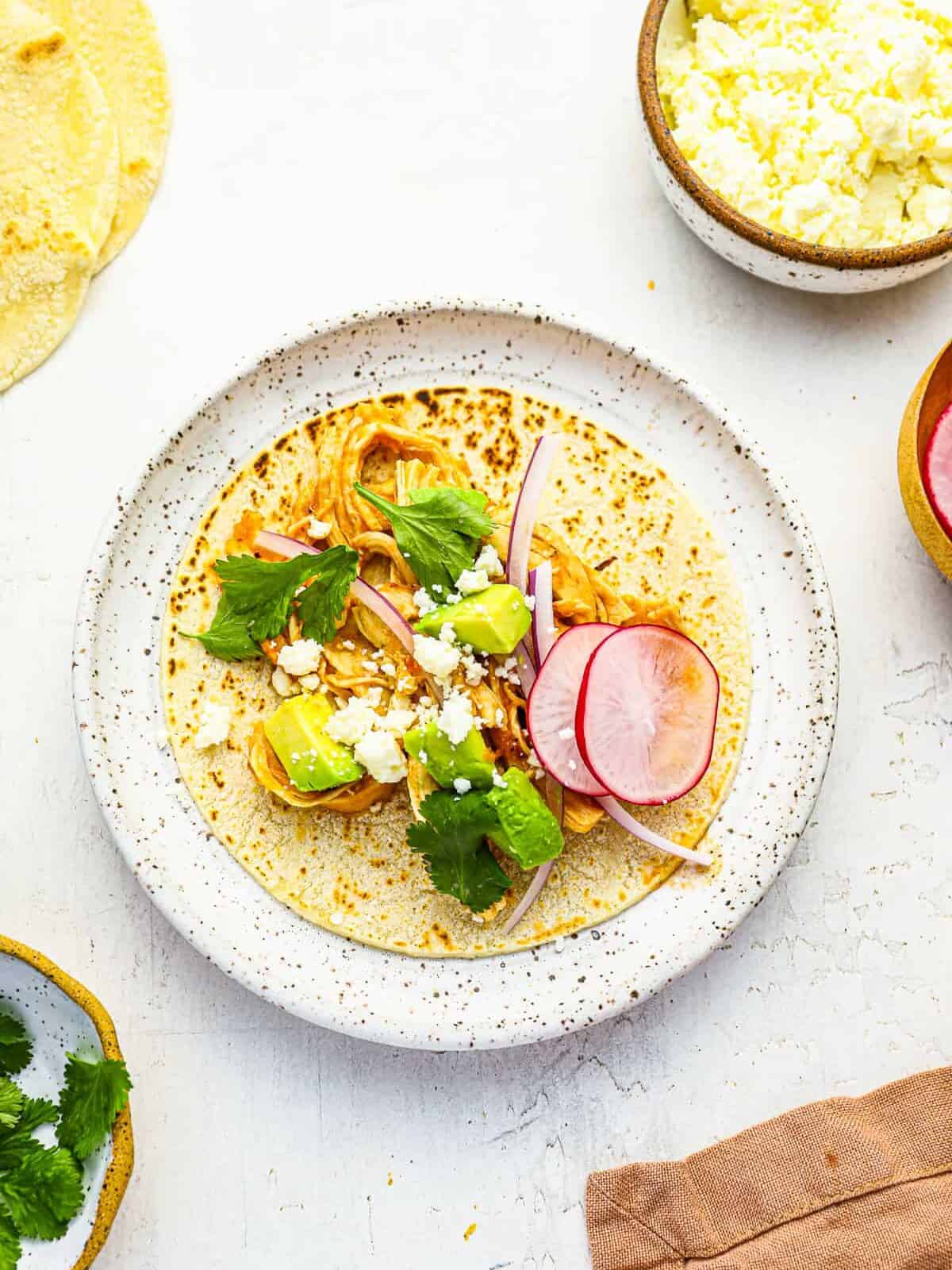 overhead view of a chicken tinga taco laid flat on a speckled white plate.