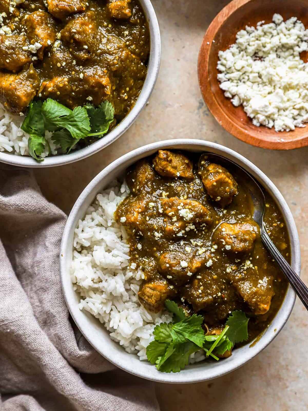 close up overhead view of 2 bowls of pork chile verde with forks and white rice.