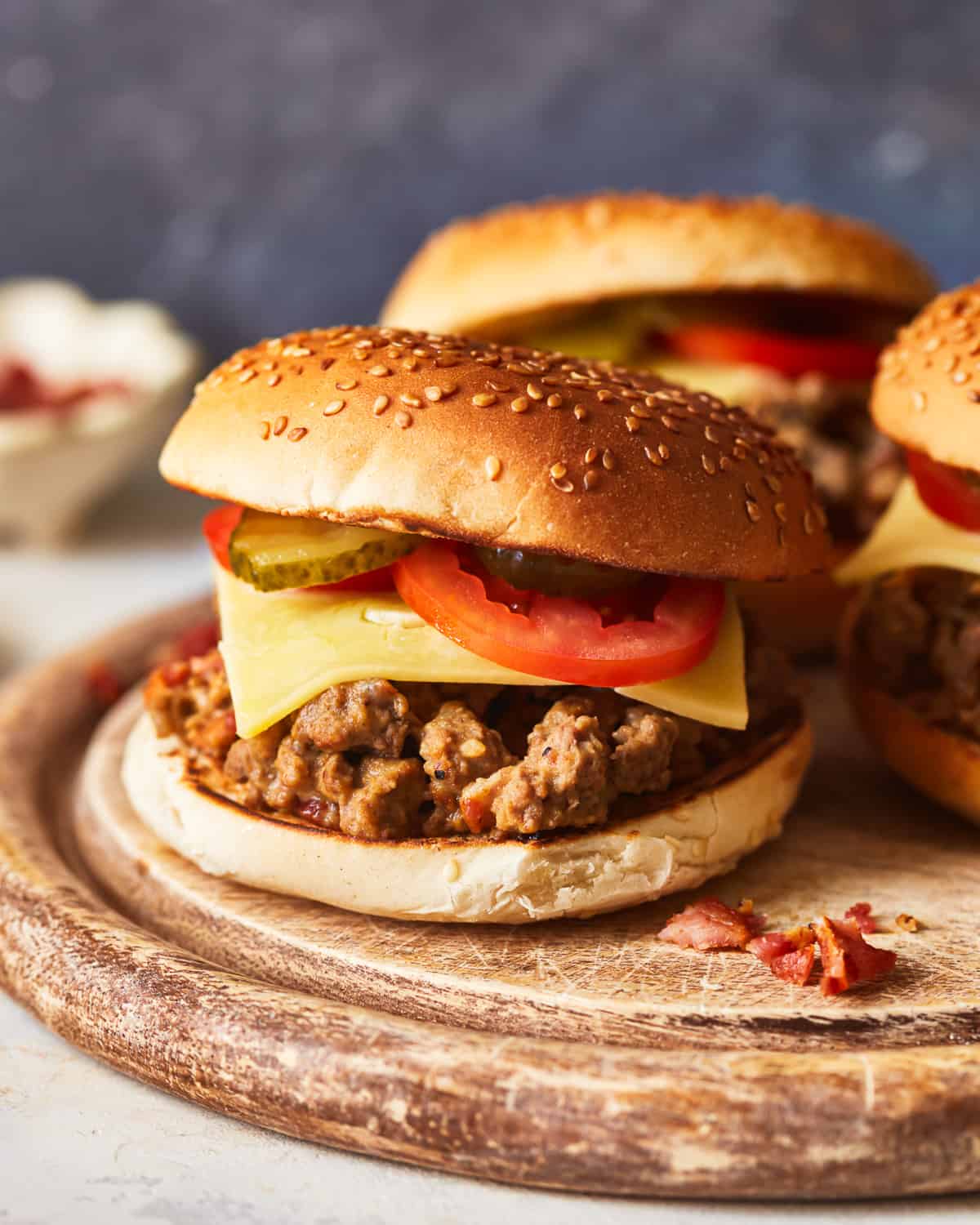 side view of crockpot cheeseburgers on a round wooden cutting board.