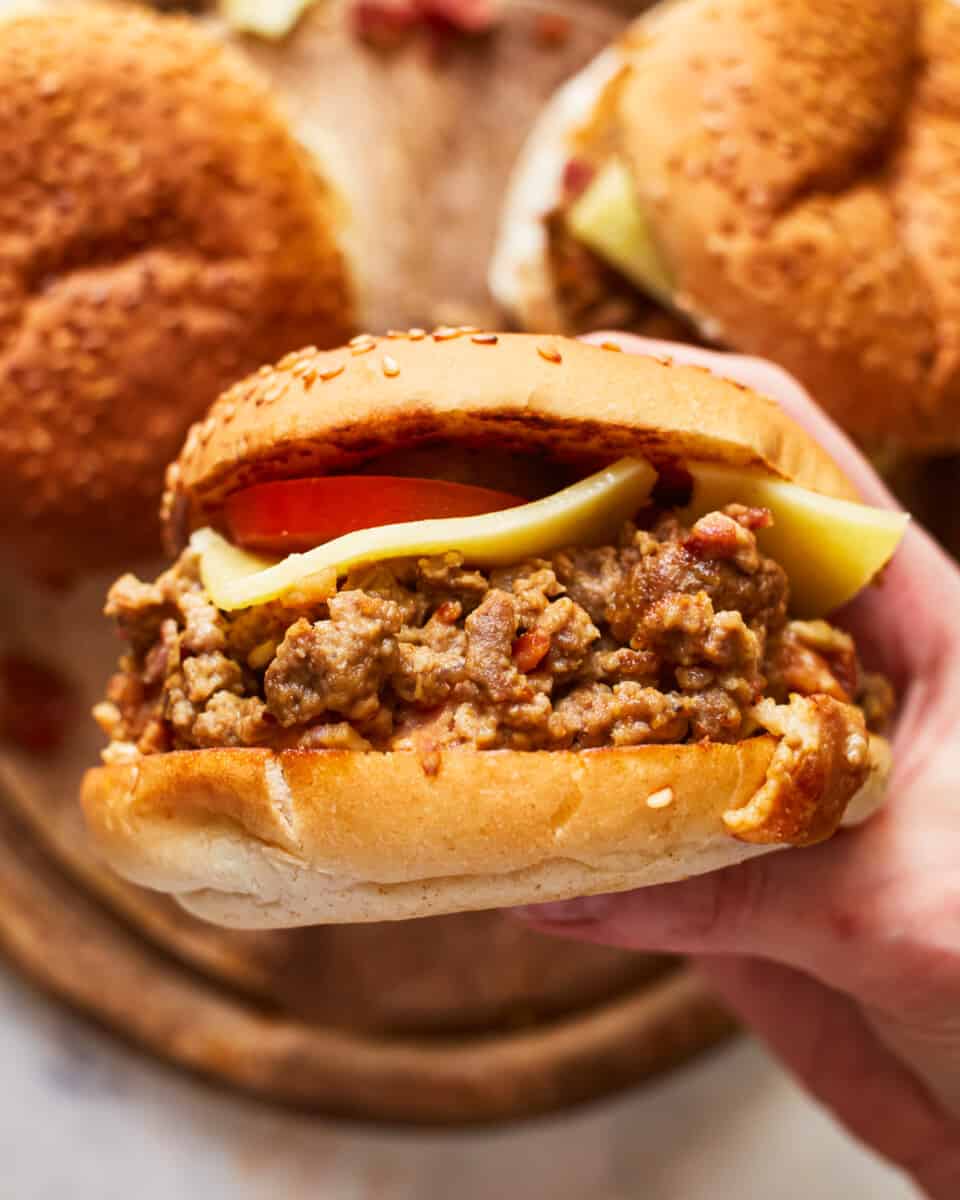 a hand holding a crockpot cheeseburger sideways to show the filling.