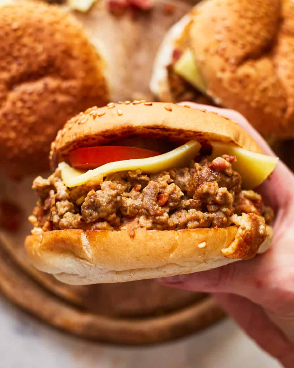 a hand holding a cheeseburger sloppy joe sideways to show the filling.