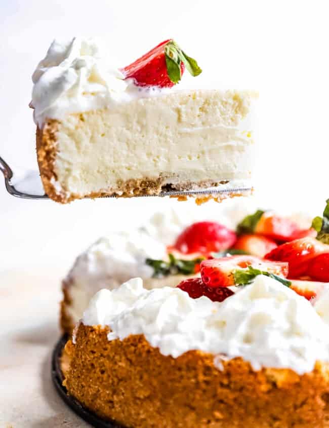 side view of a slice of easy cheesecake being lifted on a cake server from a whole cheesecake.