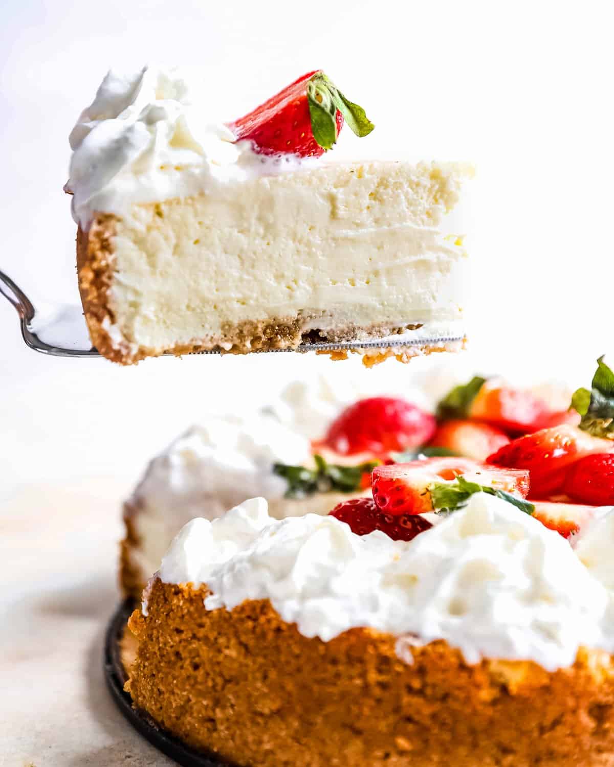 side view of a slice of easy cheesecake being lifted on a cake server from a whole cheesecake.