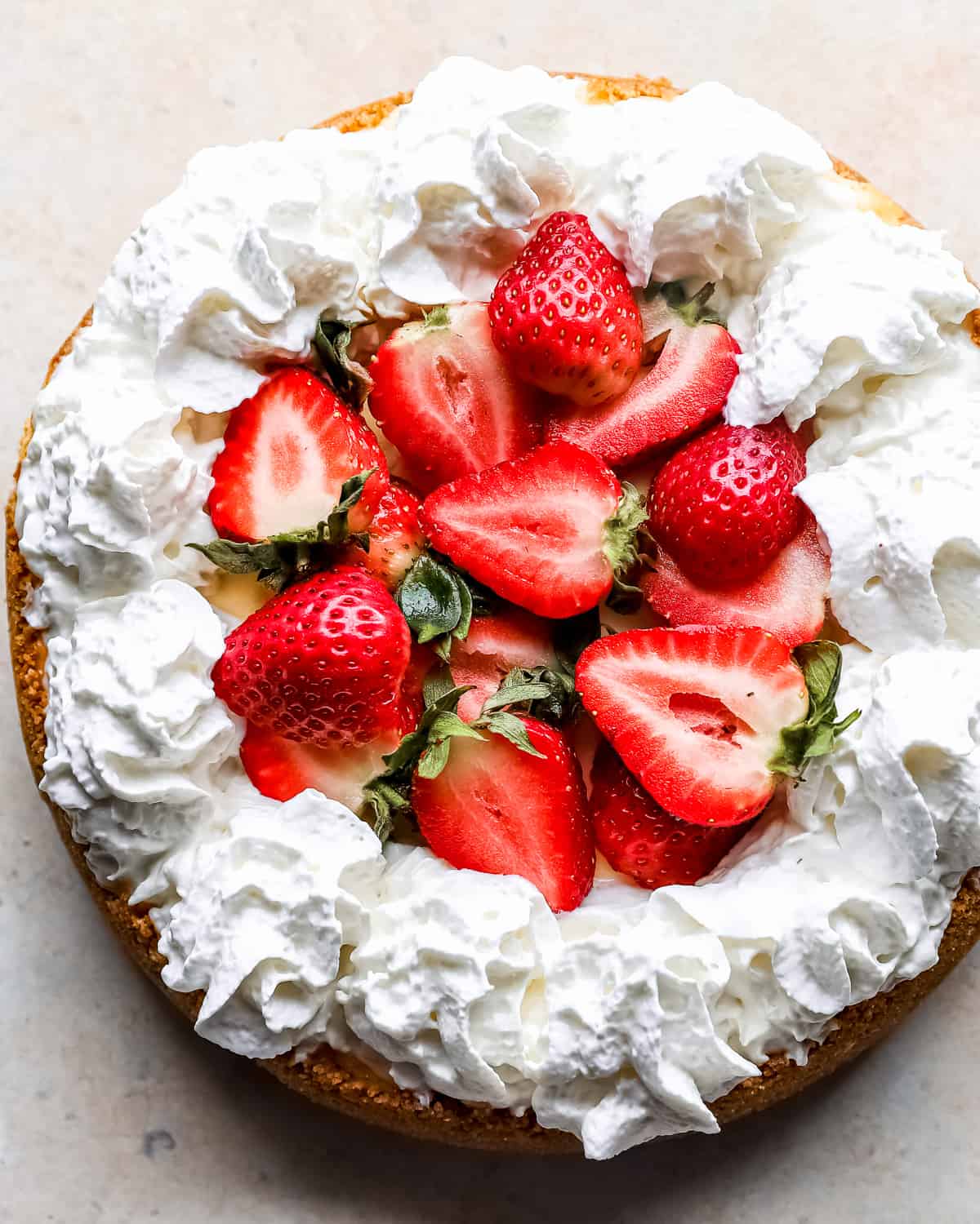 overhead view of an easy cheesecake recipe with piped whipped cream around the edges and halved strawberries in the middle.