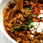 pulled pork in a white bowl with a wooden spoon.