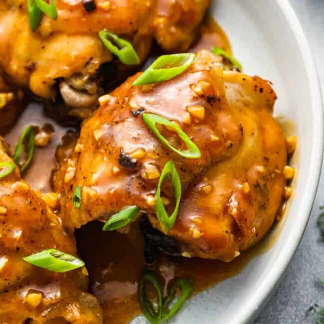chicken thighs with sauce and green onions on a plate.