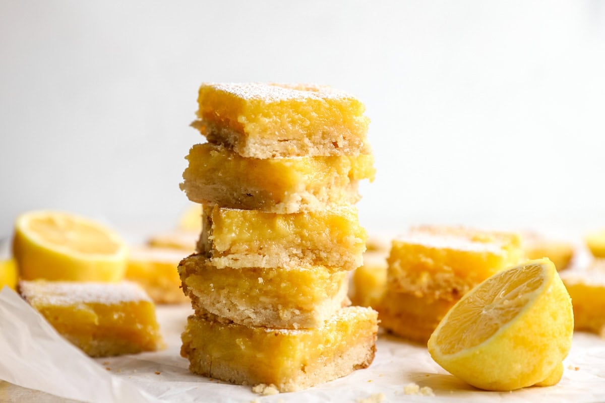 Stacked gluten-free lemon bars with fresh lemon halves on parchment paper