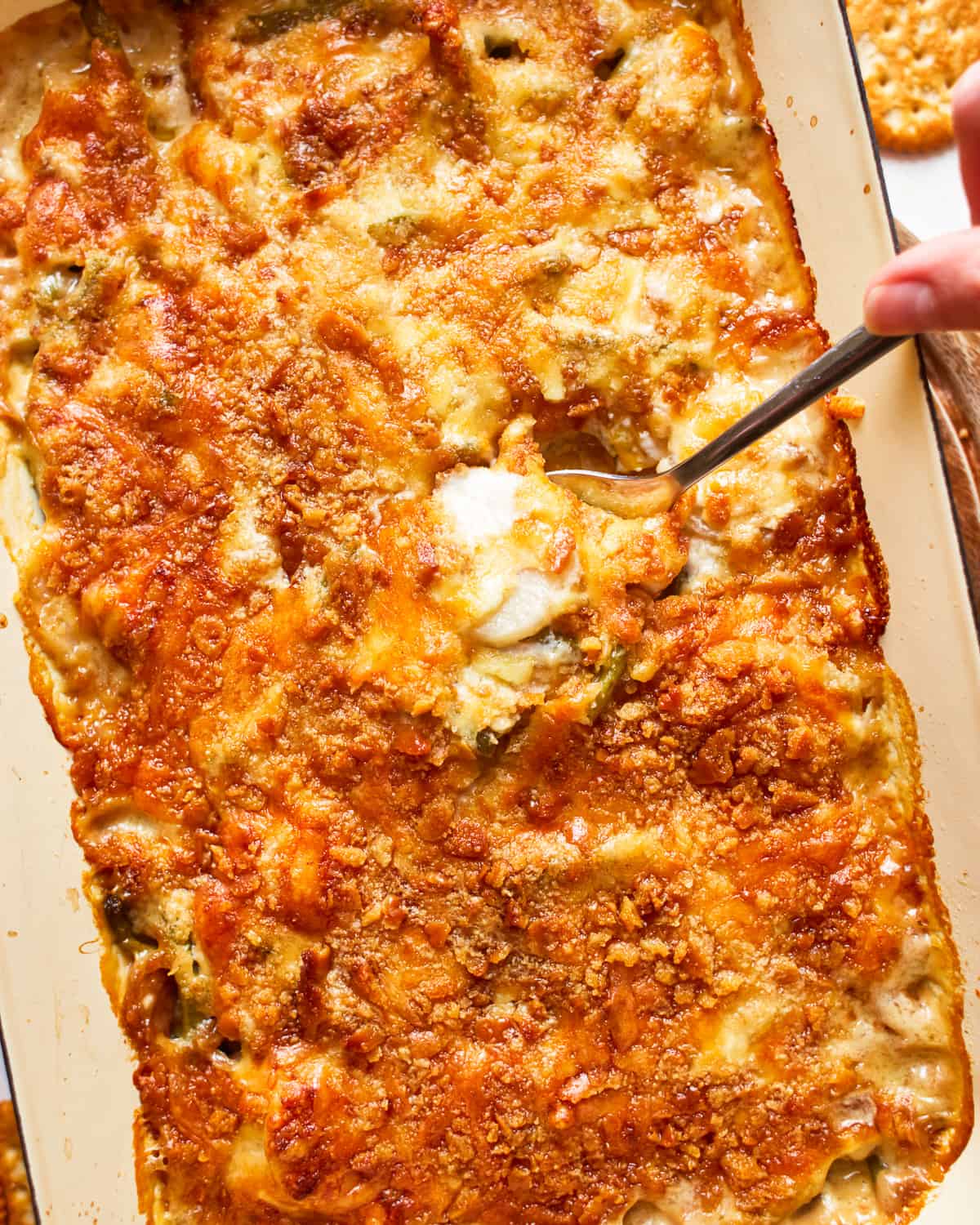 spoon digging into green bean and corn casserole with golden brown, cheesy, cracker topping