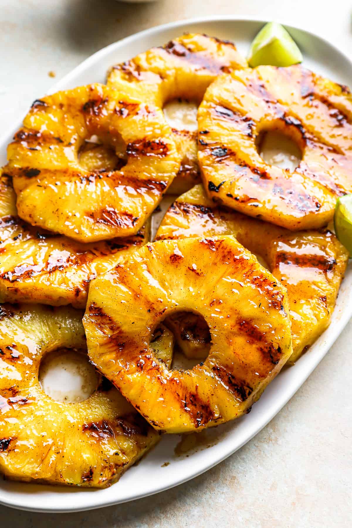 close-up three-quarters view of slices of grilled and glazed pineapple on a white oval serving platter with lime wedges.