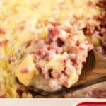 A wooden spoon scooping a serving of ham and potato casserole