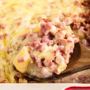 A wooden spoon scooping a serving of ham and potato casserole