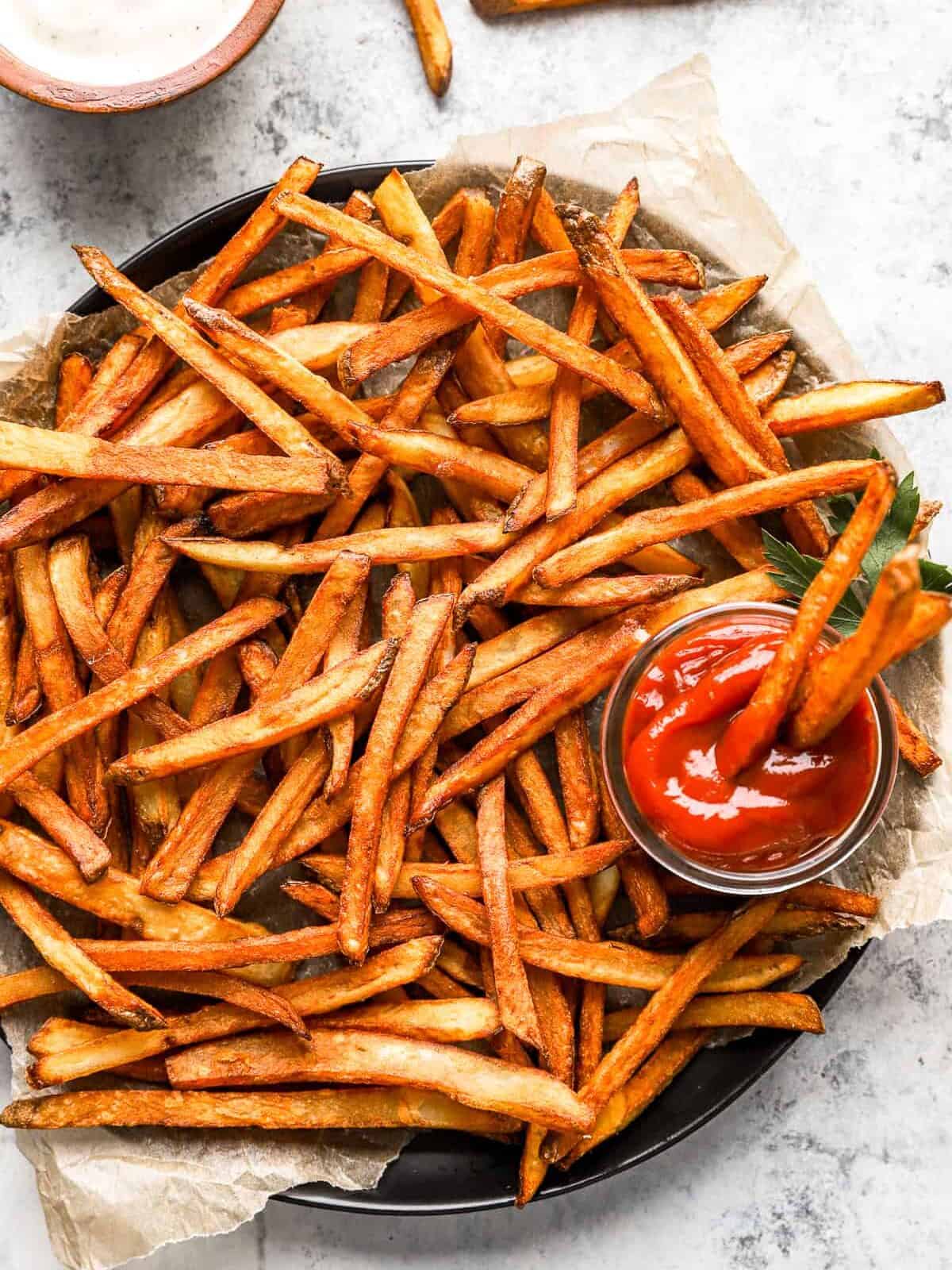 homemade french fries on a round serving tray with a cup of ketchup.