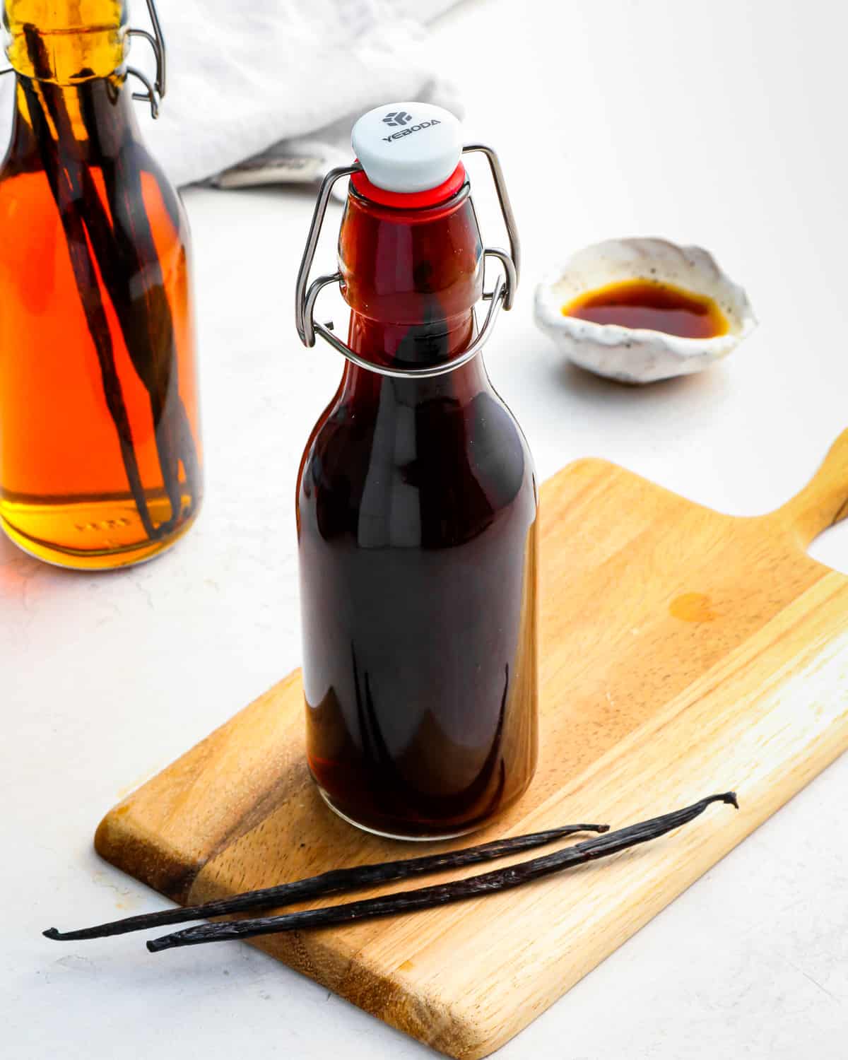a bottle of homemade vanilla extract on a wooden cutting board with 2 vanilla bean pods.
