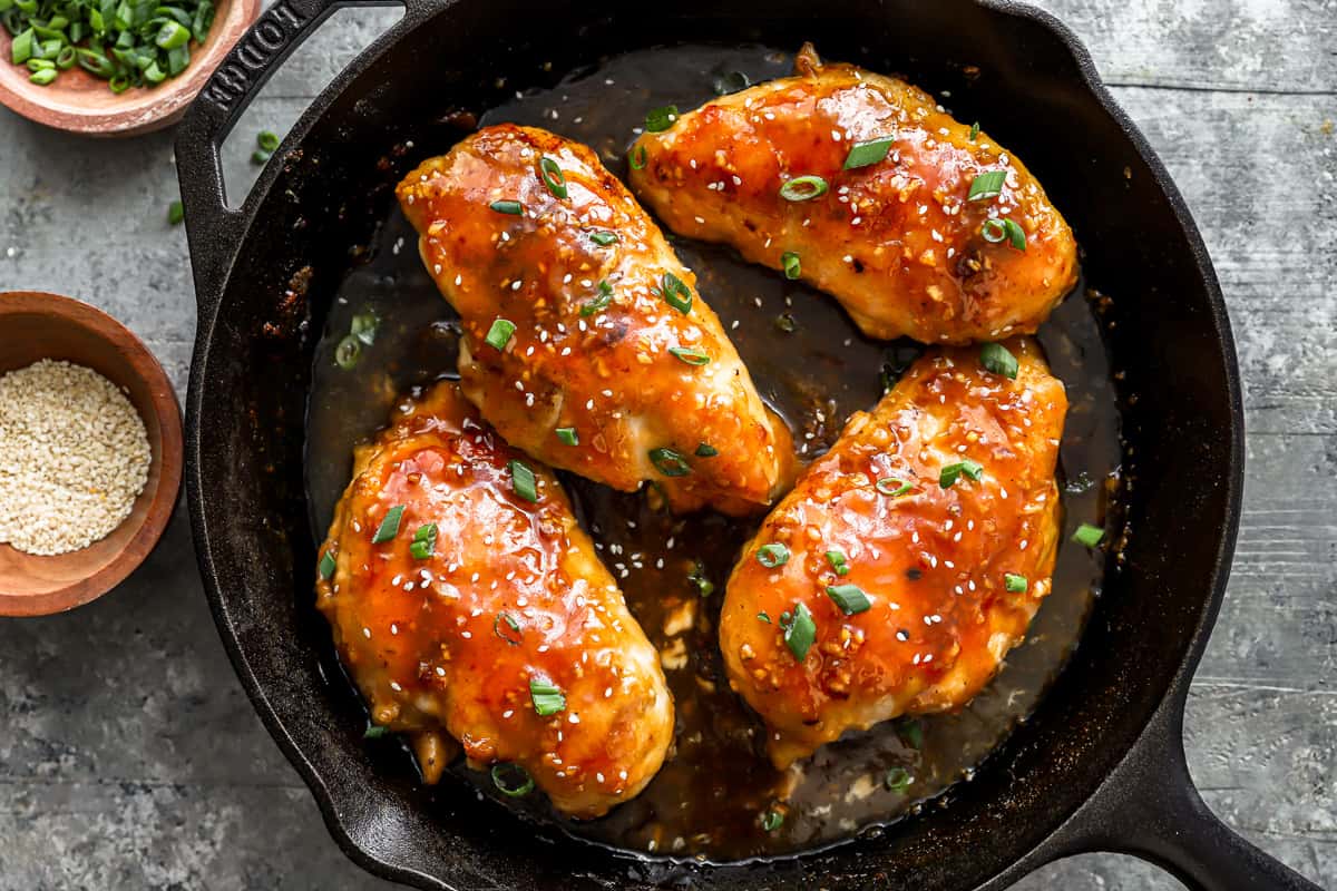 glazed chicken breasts in a skillet with sesame seeds.