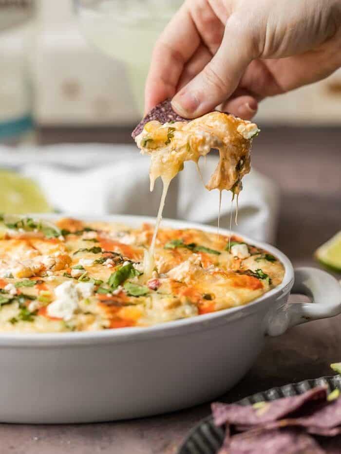 hand dipping a tortilla chip into mexican street corn dip