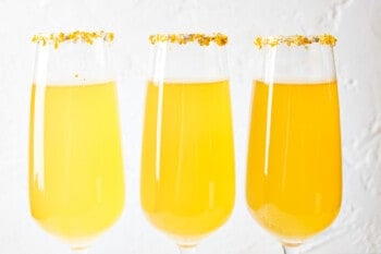 three champagne flutes filled with apple cider mimosas