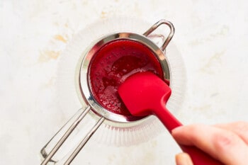 blackberry puree mixture being pressed through a fine mesh sieve with a rubber spatula.