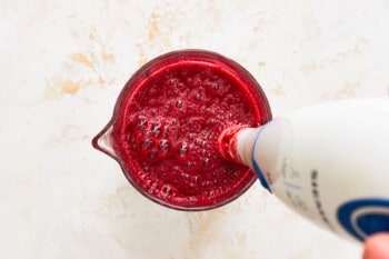 an immersion blender blending blackberries, lime juice, and chiles in a small glass cup.