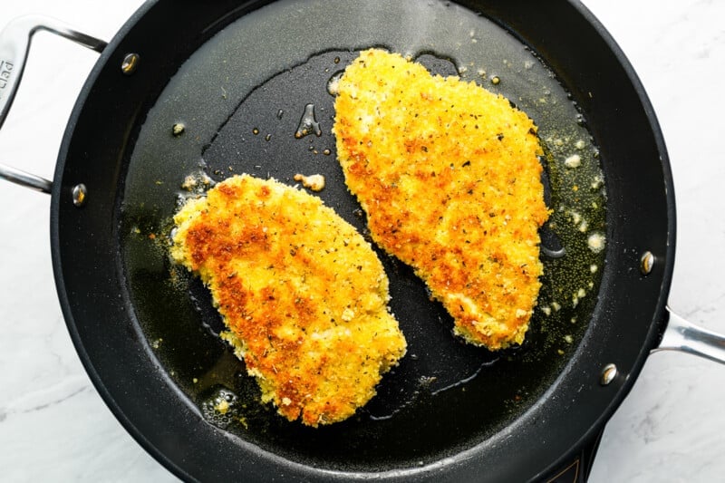 two fried chicken breasts in a frying pan.