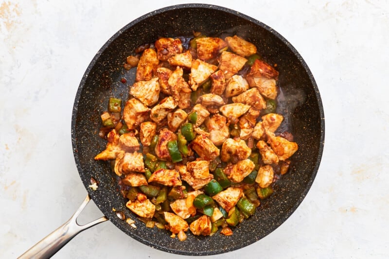 chicken, bell peppers, and onions cooking in a skillet