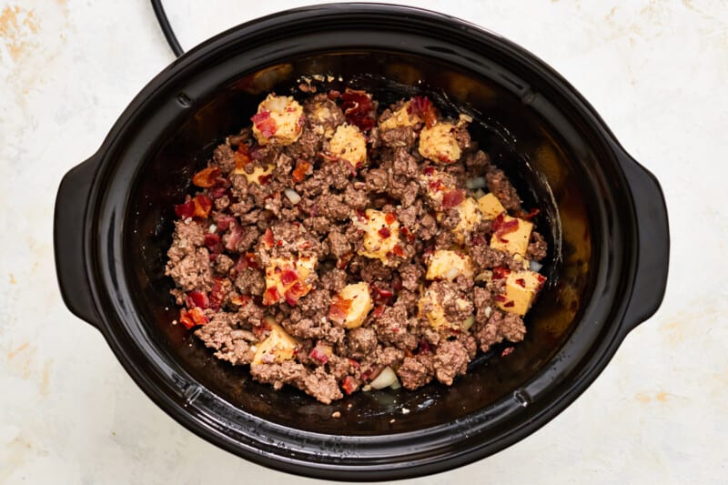 velveeta chunks and bacon added to hamburger meat in a crockpot.