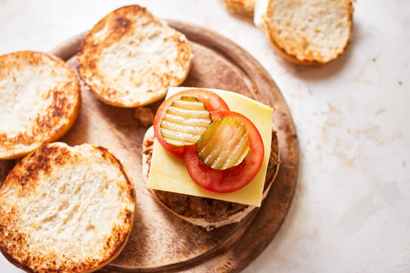 cheese, tomatoes, and pickles on top of crockpot cheeseburger meat on a hamburger bun.