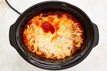 a crock pot filled with lasagna and cheese.
