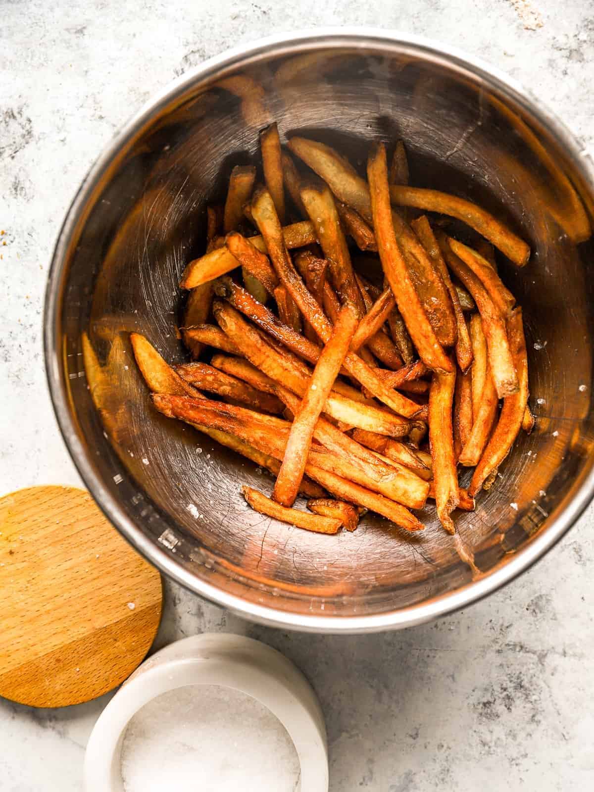 homemade french fries in a stainless steel bowl with salt.