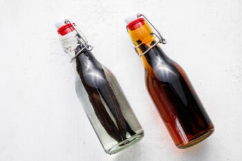 2 bottles of homemade vanilla extract, the left bottle has just started the infusion process and is clear, and the right bottle is partway through infusion and medium brown in color.