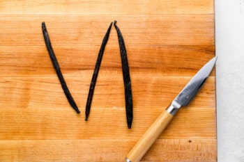 a pairing knife next to 3 vanilla beans on a wooden cutting board.