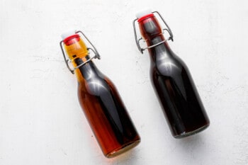 2 bottles of homemade vanilla extract, the left bottle is partway through the infusion process and medium brown in color, while the right bottle has finished infusing and is dark brown in color.