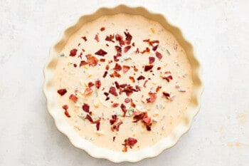 hot corn and bacon cheese dip in a white round baking dish with bacon sprinkled on top.