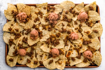 dollops of refried beans over ground beef and chips on a baking sheet.