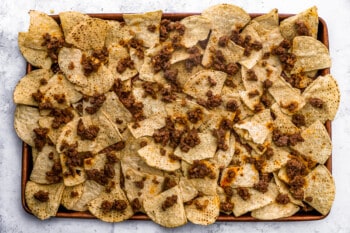 ground beef sprinkled over tortilla chips on a baking sheet.