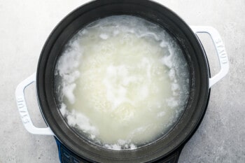 rice, water, and salt simmering in a black and white dutch oven.