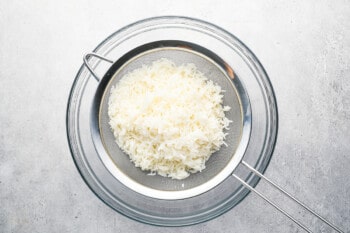 cooked basmati rice strained into a fine-mesh sieve set over a glass bowl.
