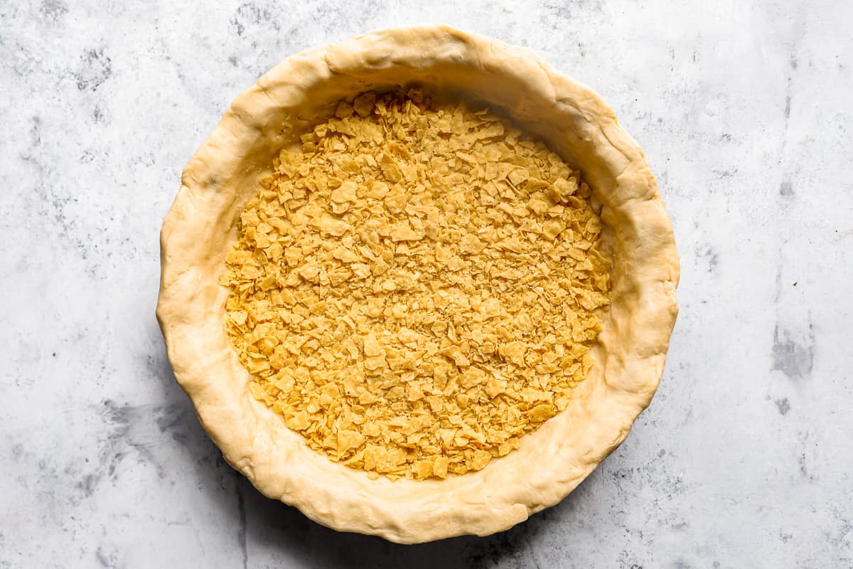 Crushed tortilla chips on top of crescent roll dough in a pie pan.