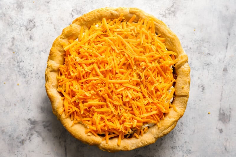 cheddar cheese sprinkled over taco pie in a pie pan.