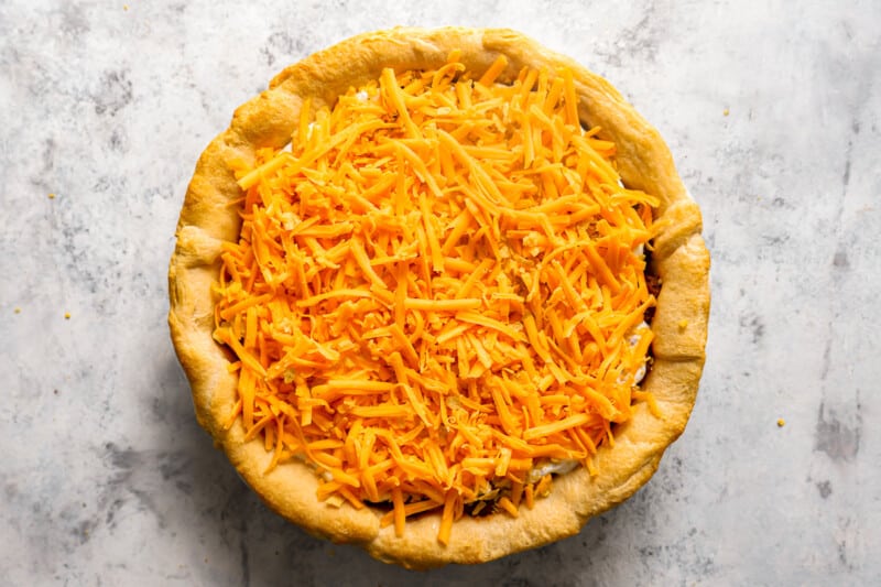 cheddar cheese sprinkled over taco pie in a pie pan.