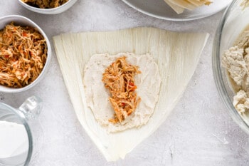 shredded chicken placed in the center of masa mixture spread over a corn husk.