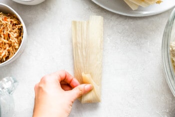 a hand folding up the bottom of a corn husk over the folded-in sides.