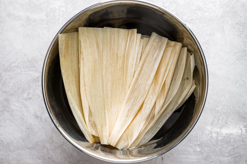 corn husks soaking in water in a stainless bowl.