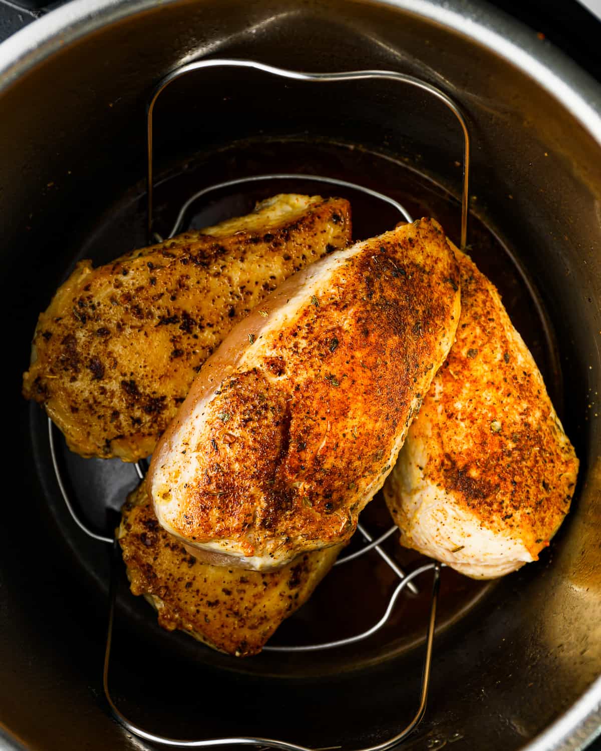 overhead view of 4 seasoned chicken breasts on a trivet in an instant pot.