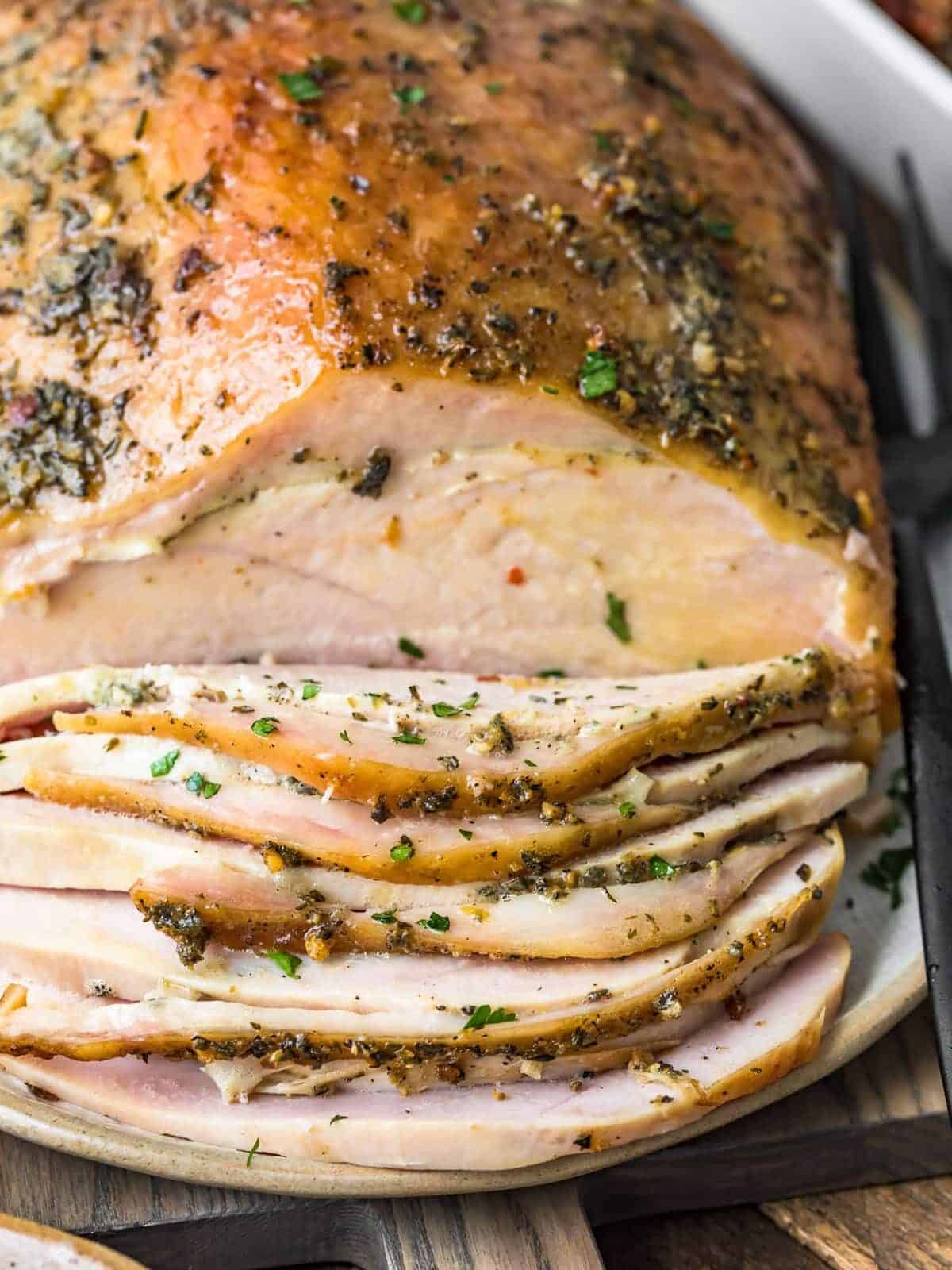 a smoked turkey breast covered in herb butter, partially sliced at the front