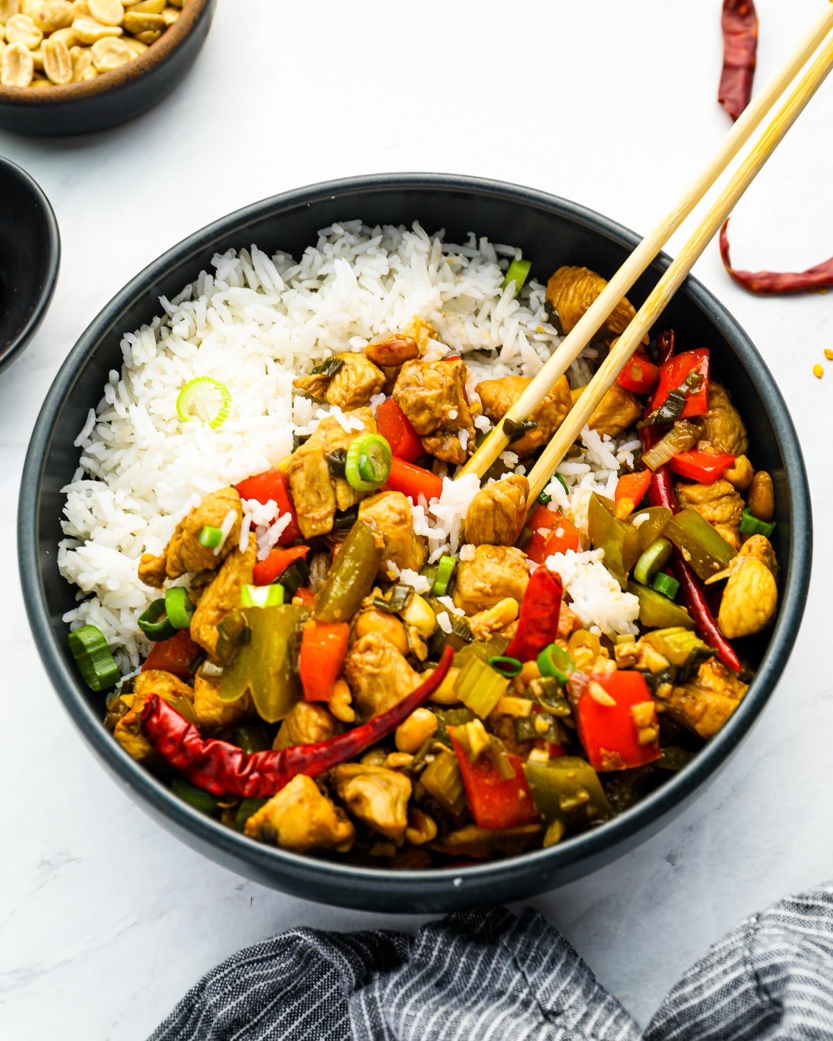 kung pao chicken stir fry in a black bowl with rice and chopsticks.