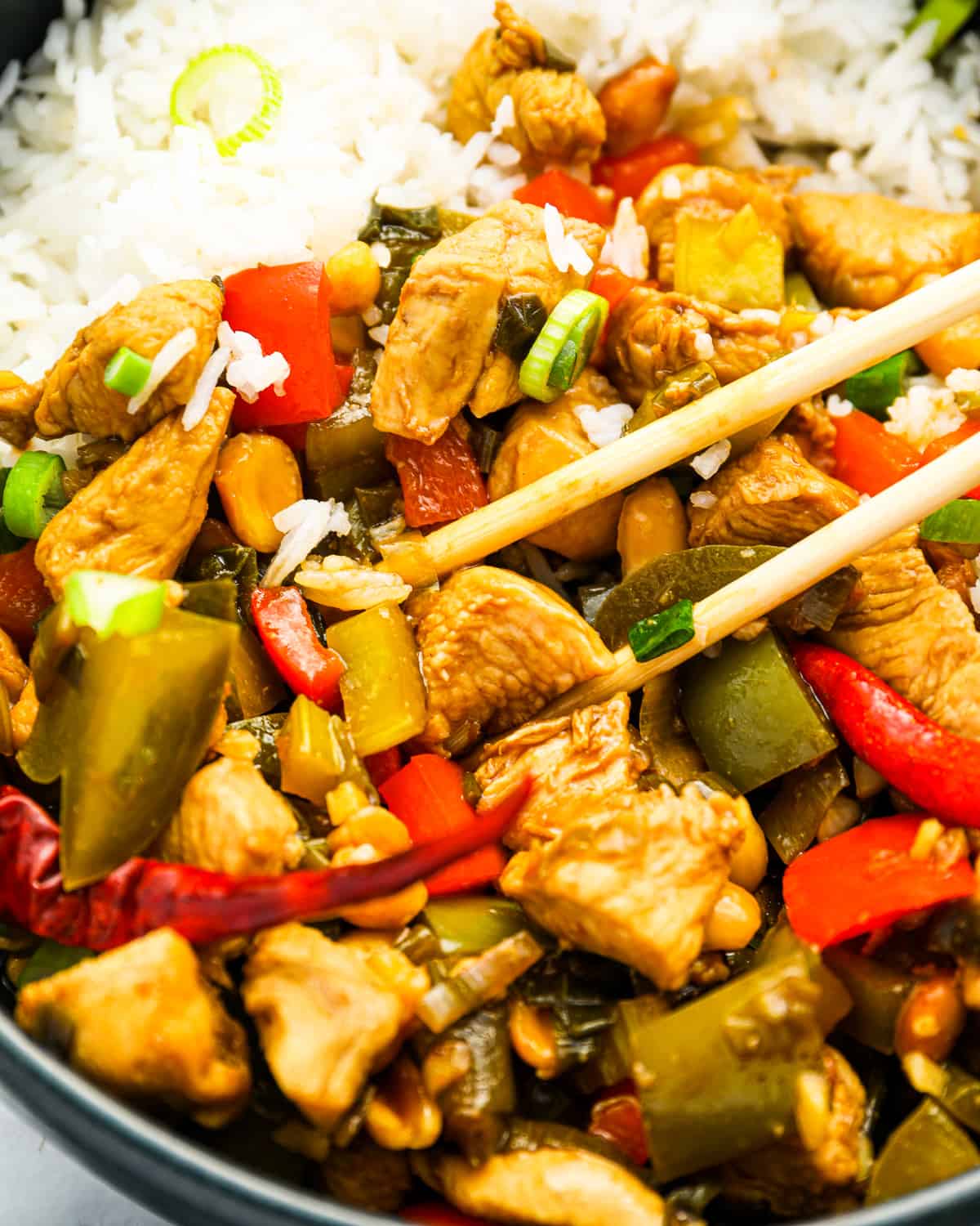 chinese chicken stir fry in a bowl with rice and chopsticks.