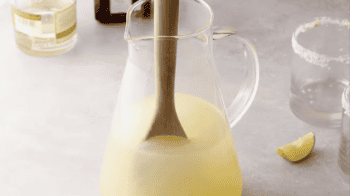 stirring margarita mixture in a pitcher with a wooden spoon.