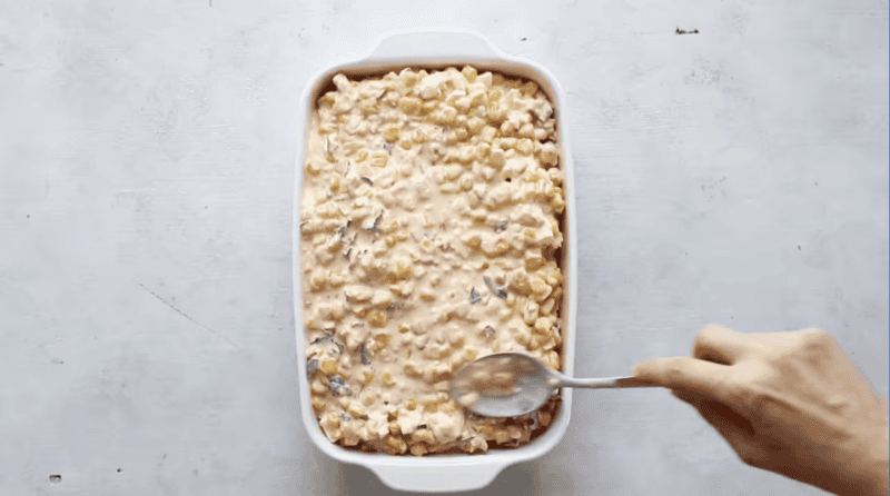 spreading mexican street corn dip in a baking pan.